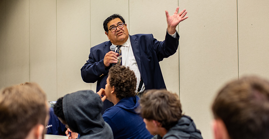 Man in business suits gestures while addressing a crowd of college students