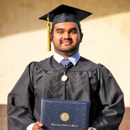Young man with black graduation garb and degree in hand.